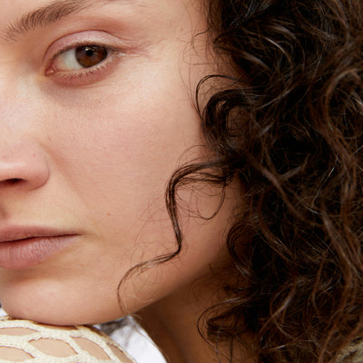 Close-up of a woman's face with dark curly hair, resting her chin on her shoulder