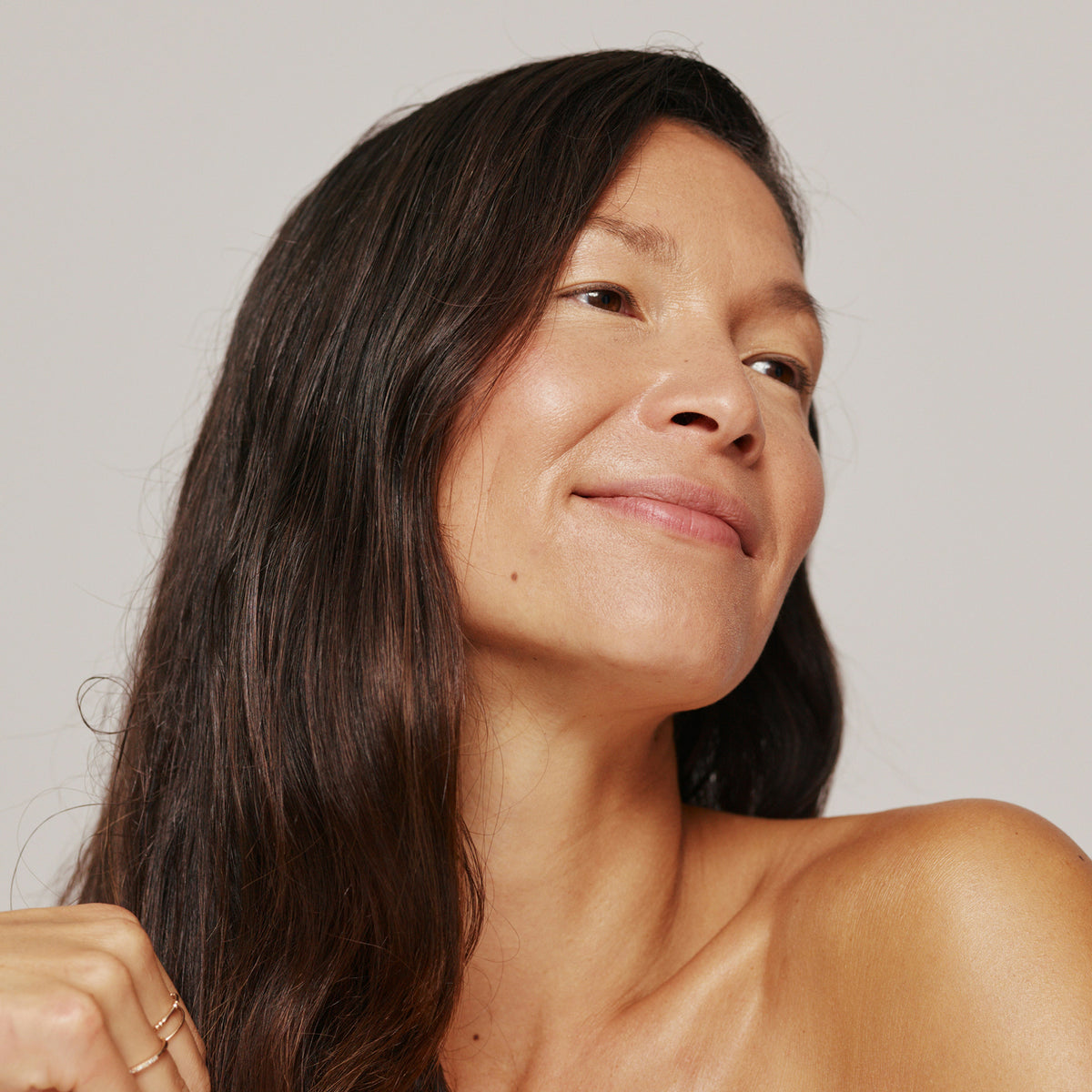 Smiling woman with long dark hair and bare shoulders looking to the side